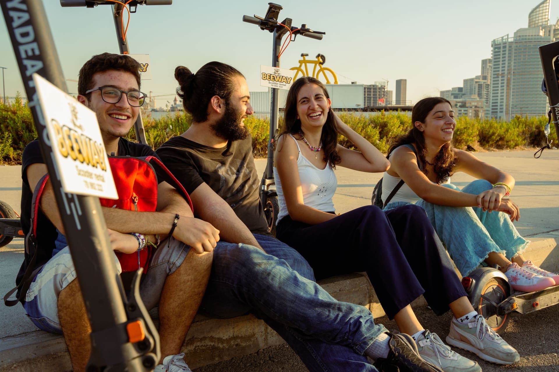 Riders sitting with their BeeWay electric scooters on the Beirut waterfront at sunset